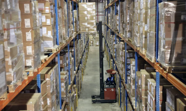 A female worker is driving a forklift onto the shelves.