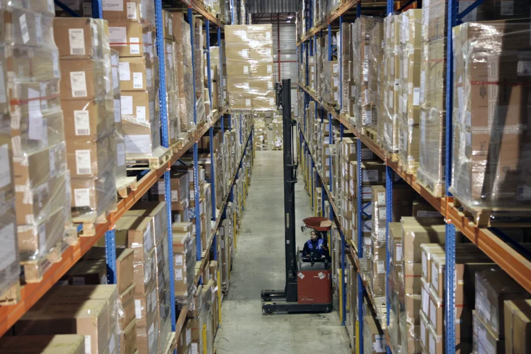 A female worker is driving a forklift onto the shelves.